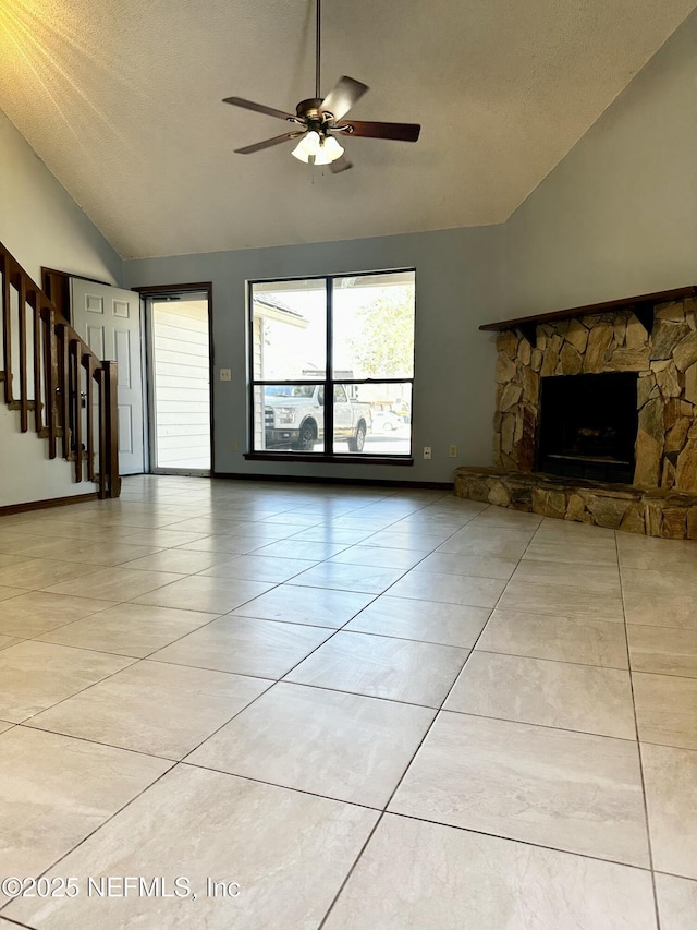 unfurnished living room with lofted ceiling, a stone fireplace, a textured ceiling, light tile patterned floors, and ceiling fan