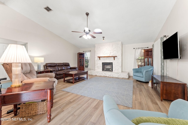 living room featuring a stone fireplace, plenty of natural light, light hardwood / wood-style floors, and ceiling fan