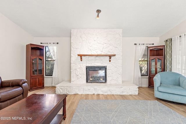 living room featuring vaulted ceiling, a fireplace, and light hardwood / wood-style floors