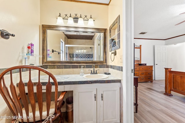 bathroom with a shower with shower door, hardwood / wood-style flooring, vanity, crown molding, and a textured ceiling