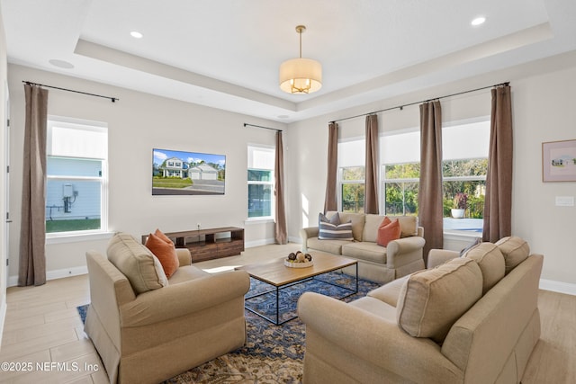 living room with light wood-type flooring, baseboards, a tray ceiling, and recessed lighting