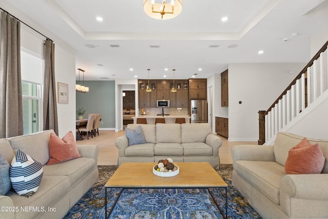 living area featuring stairs, a tray ceiling, recessed lighting, and light wood-style floors