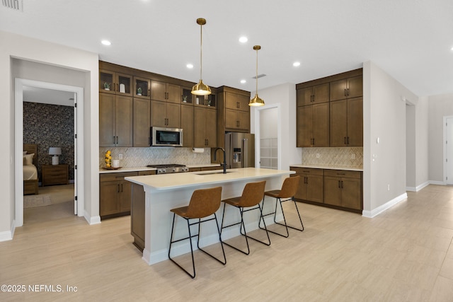 kitchen featuring an island with sink, a breakfast bar, stainless steel appliances, light countertops, and a sink