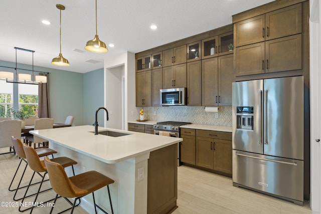 kitchen with tasteful backsplash, high end appliances, an island with sink, a breakfast bar area, and a sink