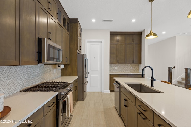 kitchen with pendant lighting, stainless steel appliances, light countertops, visible vents, and a sink