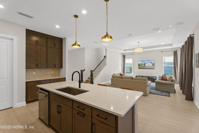 kitchen with a sink, visible vents, light countertops, a tray ceiling, and tasteful backsplash