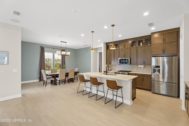 kitchen featuring visible vents, light countertops, appliances with stainless steel finishes, backsplash, and a center island with sink