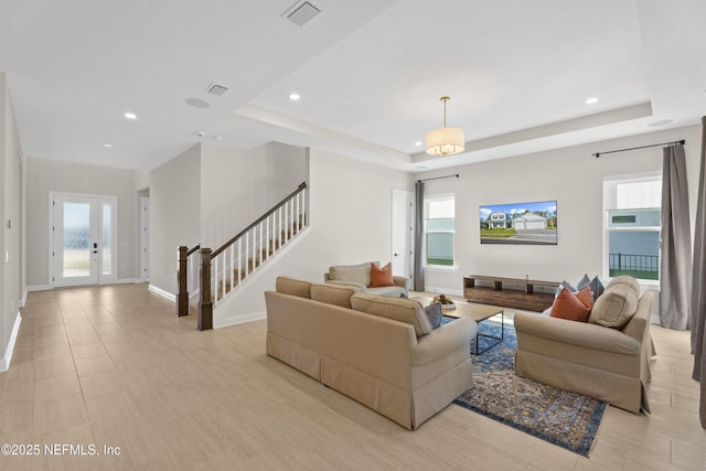 living area with stairway, visible vents, a tray ceiling, and baseboards