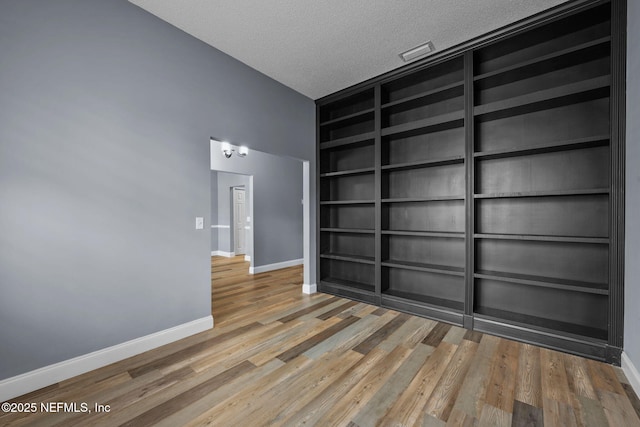 spare room with built in shelves, a textured ceiling, and hardwood / wood-style flooring