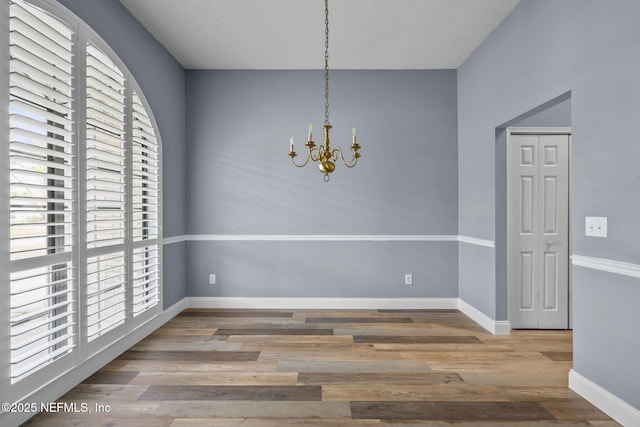 unfurnished dining area with an inviting chandelier, hardwood / wood-style floors, and a textured ceiling