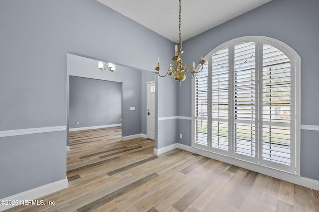 spare room featuring an inviting chandelier, hardwood / wood-style flooring, and a textured ceiling