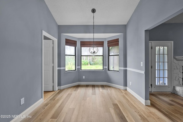 unfurnished dining area with light wood-type flooring, a notable chandelier, and a textured ceiling