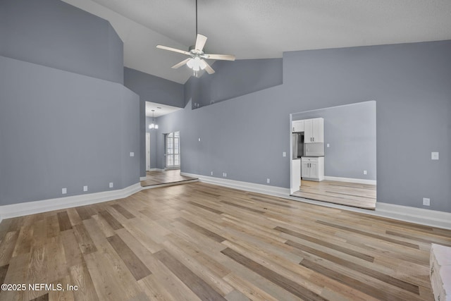 unfurnished living room with ceiling fan with notable chandelier, high vaulted ceiling, and light hardwood / wood-style flooring