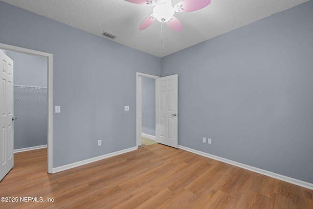 unfurnished bedroom with a spacious closet, a textured ceiling, a closet, ceiling fan, and light hardwood / wood-style floors