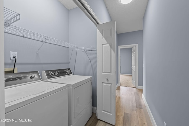 laundry area with light wood-type flooring, washer and dryer, and a textured ceiling