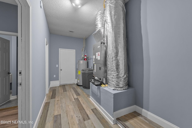 hallway with electric water heater, a textured ceiling, and light hardwood / wood-style flooring