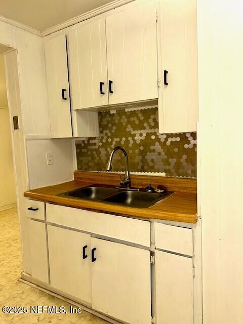 kitchen with white cabinetry, crown molding, sink, and backsplash