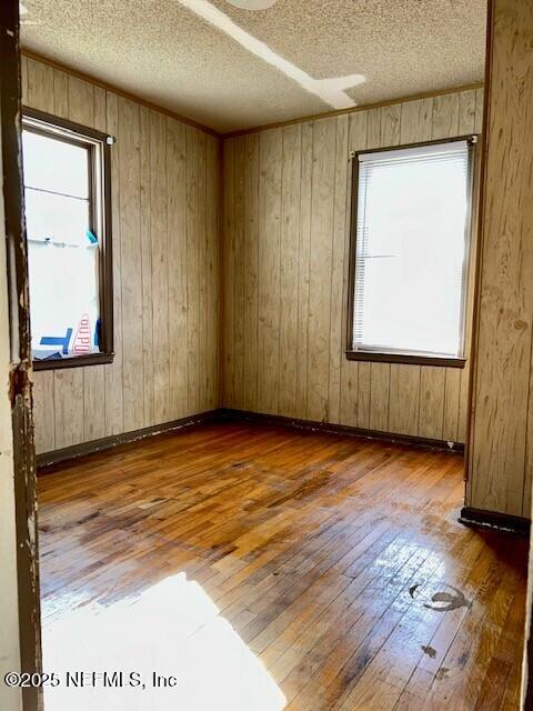 spare room with hardwood / wood-style flooring, plenty of natural light, wooden walls, and a textured ceiling