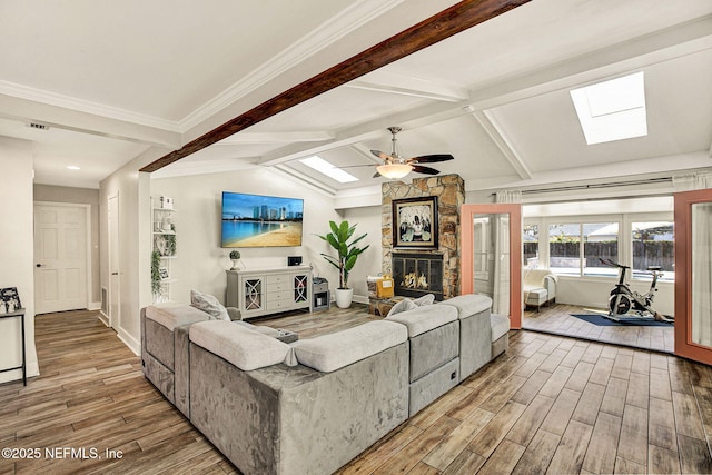 living room with vaulted ceiling with skylight, a stone fireplace, hardwood / wood-style floors, and ceiling fan