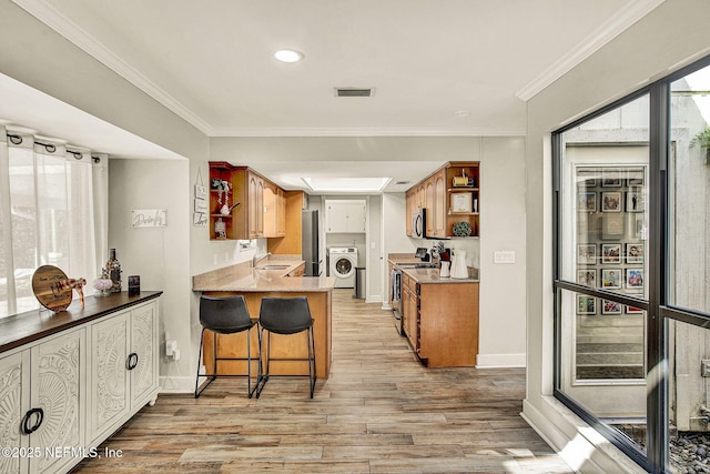 kitchen featuring washer / clothes dryer, sink, a kitchen bar, kitchen peninsula, and stainless steel appliances