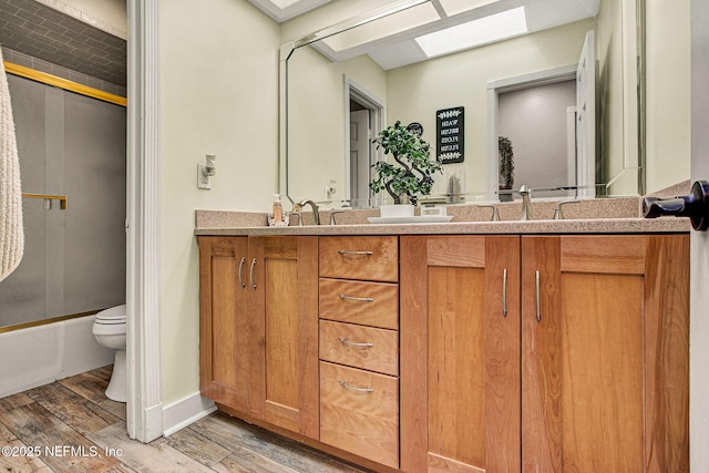 full bathroom with hardwood / wood-style floors, a skylight, shower / bath combination with glass door, vanity, and toilet