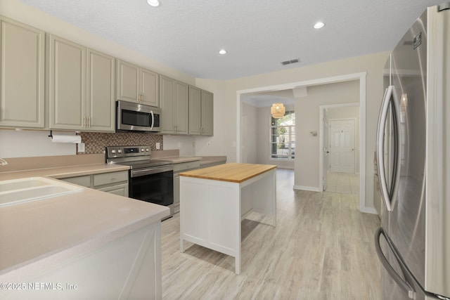 kitchen with butcher block counters, sink, a textured ceiling, a kitchen island, and stainless steel appliances