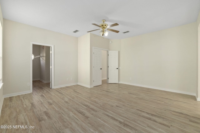 unfurnished bedroom featuring ceiling fan, a spacious closet, a closet, and light wood-type flooring