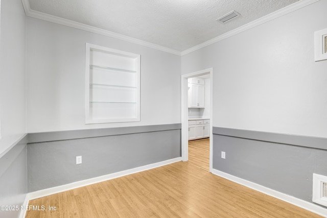 spare room featuring crown molding, built in shelves, a textured ceiling, and light wood-type flooring