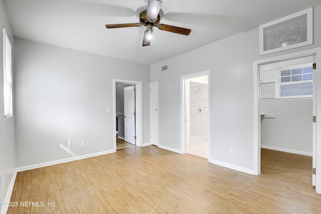 unfurnished bedroom with a closet, a spacious closet, ensuite bath, and light hardwood / wood-style flooring