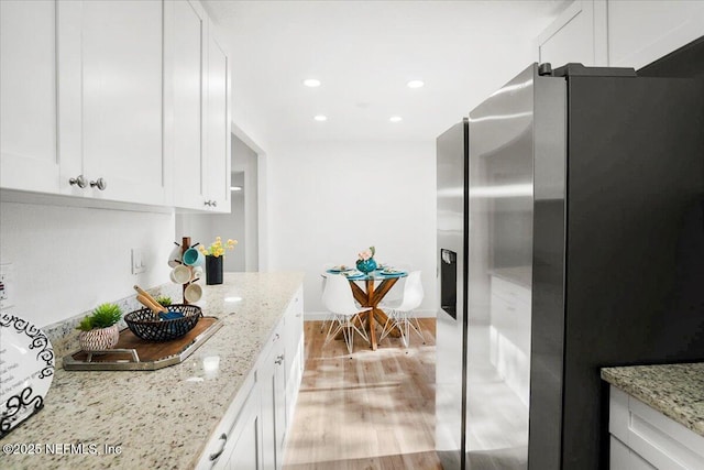 kitchen featuring white cabinets, stainless steel fridge, light stone counters, and light hardwood / wood-style flooring