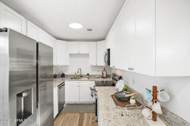 kitchen featuring sink, white cabinets, light hardwood / wood-style floors, stainless steel appliances, and light stone countertops