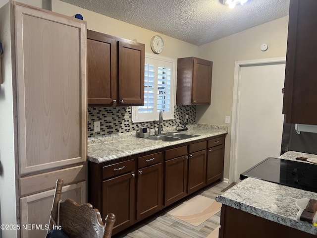 kitchen with sink, light hardwood / wood-style flooring, range, backsplash, and dark brown cabinets