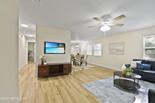 living room featuring ceiling fan, a textured ceiling, and light wood-type flooring