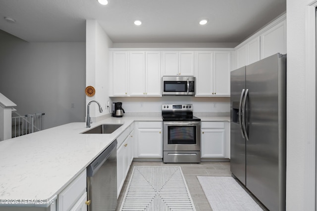 kitchen with sink, white cabinetry, stainless steel appliances, light stone counters, and kitchen peninsula