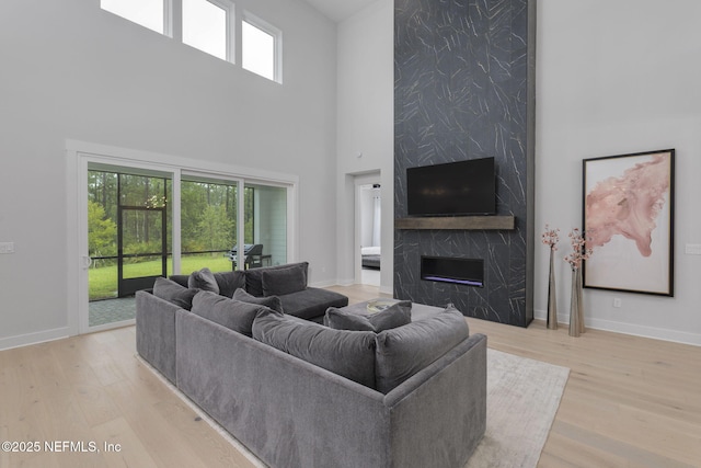 living room featuring light wood-type flooring, a high end fireplace, and a towering ceiling