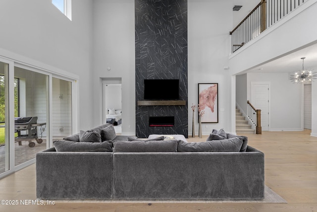 living room featuring a towering ceiling, an inviting chandelier, a fireplace, and light hardwood / wood-style flooring