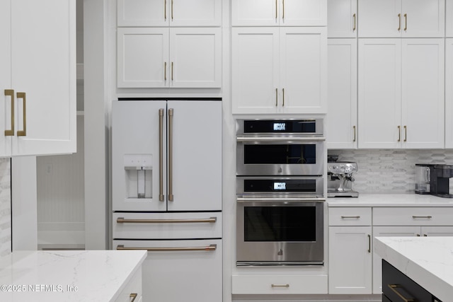 kitchen featuring high end white refrigerator, stainless steel double oven, white cabinets, and light stone counters