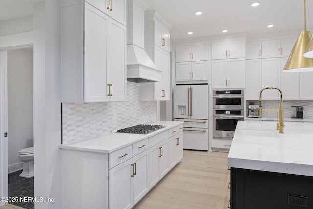 kitchen with decorative light fixtures, custom range hood, white cabinets, and appliances with stainless steel finishes