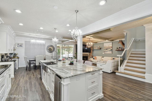 kitchen featuring pendant lighting, a fireplace, sink, white cabinets, and a kitchen island with sink