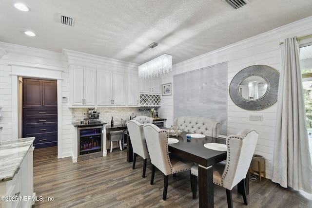 dining room with beverage cooler, crown molding, dark wood-type flooring, a textured ceiling, and an inviting chandelier