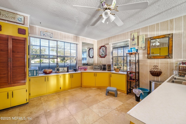 kitchen featuring light tile patterned flooring, sink, a textured ceiling, wooden walls, and ceiling fan