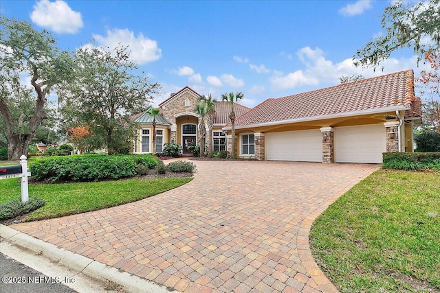 view of front of property with a front lawn, a tile roof, decorative driveway, stone siding, and an attached garage