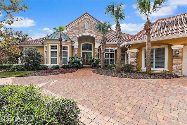 mediterranean / spanish-style home with a tiled roof, stone siding, and stucco siding