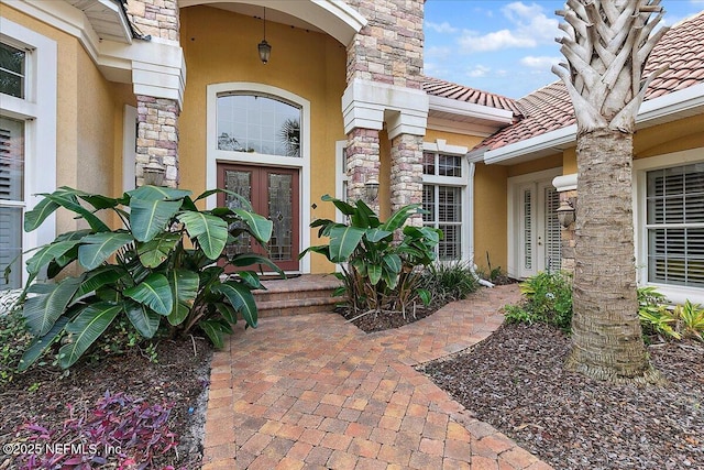 doorway to property with a tiled roof, french doors, stone siding, and stucco siding