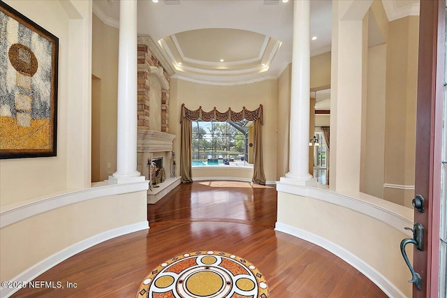 entrance foyer with wood finished floors, ornate columns, a tray ceiling, a fireplace, and crown molding