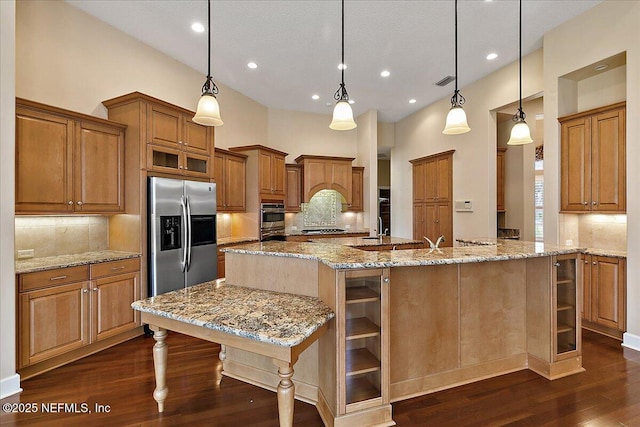 kitchen with visible vents, brown cabinets, a large island, stainless steel fridge, and dark wood-style flooring