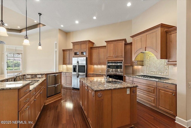 kitchen with brown cabinetry, a sink, stainless steel appliances, and a kitchen island with sink