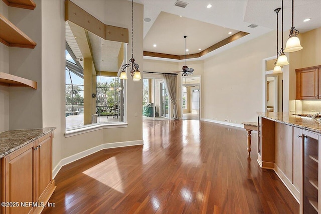 unfurnished dining area with visible vents, a raised ceiling, baseboards, and dark wood-style floors