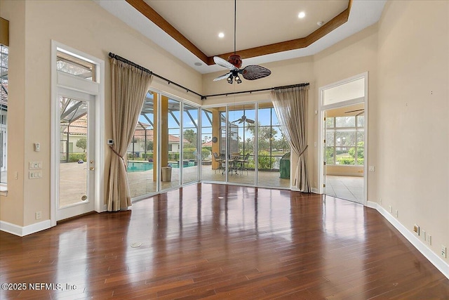 empty room featuring baseboards, a raised ceiling, wood finished floors, and a sunroom