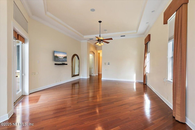 empty room featuring ornamental molding, a ceiling fan, wood finished floors, arched walkways, and a raised ceiling